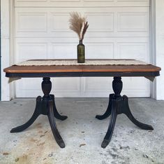 a wooden table with a vase and feather on it in front of a garage door