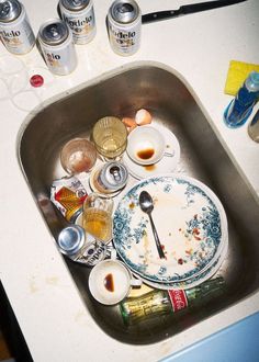 dirty dishes are sitting in the sink with empty cans on the counter top next to it