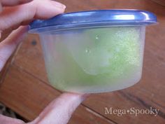 a person is holding a plastic container with green liquid in it and the lid partially open