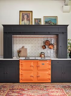 an orange stove top oven sitting in a kitchen next to a wall with pictures on it