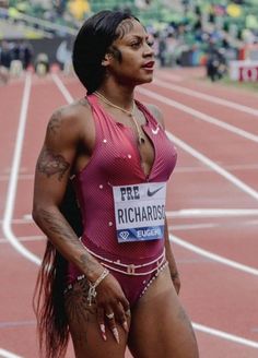 a woman standing on top of a track in a pink shirt and silver chain around her neck