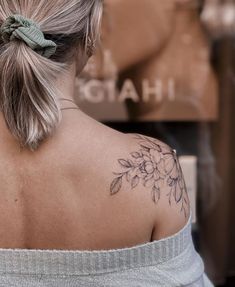 a woman with a flower tattoo on her back shoulder and behind her is a sign