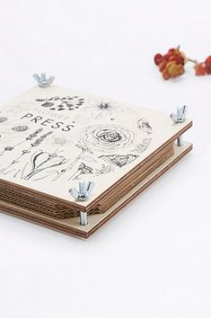 an open notebook sitting on top of a white table next to flowers and leaves with pins stuck in the pages