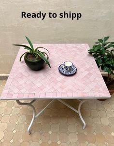 a pink table with a blue and white plate on it next to a potted plant