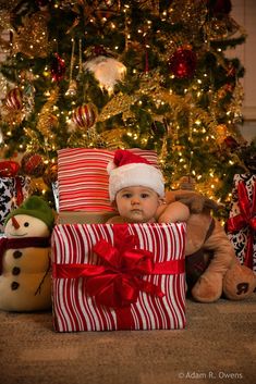 a baby wearing a santa hat and sitting in front of a christmas tree with presents