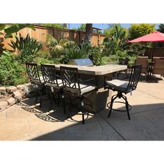 an outdoor table and chairs with umbrellas in the back yard, surrounded by plants