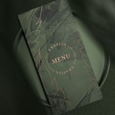 a menu cover on a black plate with green and gold leaves in the background,