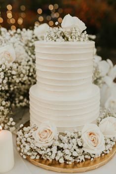 a wedding cake with white flowers and candles on the table next to it is decorated with baby's breath