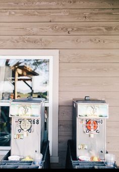 two soda machines sitting next to each other in front of a wooden wall and window