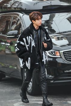 a man in black and white jacket walking down the street with his hand on his hip