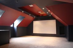 an empty room with red and black walls, white paneled ceiling and large screen on the wall