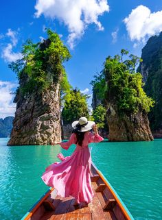 a woman in a pink dress and hat riding on a boat through the blue water