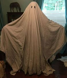 a large white cloth covered ghost sitting on top of a wooden floor next to a window