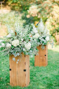 two wooden vases filled with white flowers and greenery on top of green grass