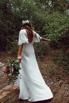 a woman in a white dress walking through the woods