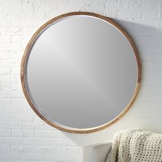 a round mirror hanging on the wall next to a white towel and a brick wall