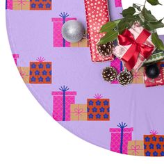 presents wrapped in paper and tied with red ribbon on a purple table cloth next to a christmas ornament