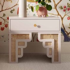 a white table with two drawers next to a wallpapered wall and potted plant