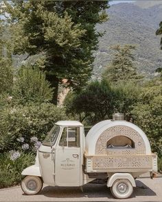 an old truck is parked in front of some trees and bushes with a pizza oven on the back