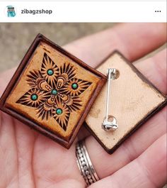 a hand holding a wooden brooch with an intricate design on it