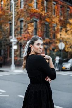 a woman is standing on the street with her arms crossed and looking off to the side