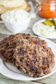 two hamburger patties on a white plate with pickles and cottage cheese in the background