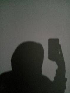 the shadow of a person holding a cell phone up to their face in front of a white wall