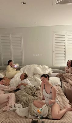 four women are laying in bed with blankets on them