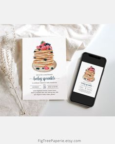 a cell phone next to a stack of pancakes on top of a white table cloth