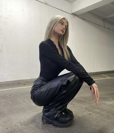 a woman kneeling down on the ground with her hands in her pockets and looking off to the side