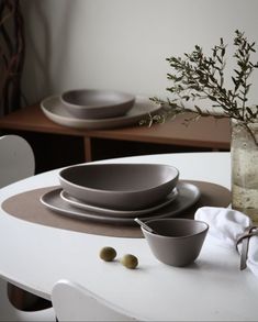 a white table topped with plates and bowls next to a vase filled with green olives