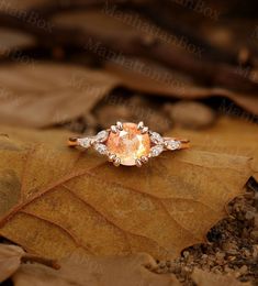 an orange and white diamond ring sitting on top of a leaf covered ground with leaves around it