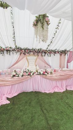 a table covered in pink cloths and flowers under a white canopy with chandelier