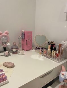 a white desk topped with lots of makeup and other items next to a pink teddy bear