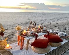 a table set up on the beach with candles, plates and flowers in vases