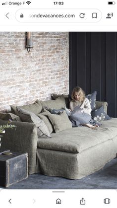 a woman sitting on top of a couch next to a brick wall