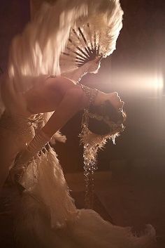 a woman dressed in white with feathers on her head and hands behind her back, posing for the camera