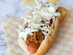 a hot dog covered in coleslaw on top of a checkered table cloth