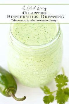 a jar filled with green sauce next to a pepper and coriant sprig