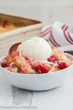 a white bowl filled with ice cream and strawberry cobbler next to a baking dish