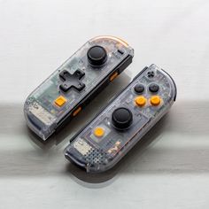 two video game controllers sitting next to each other on a white surface with yellow and black buttons