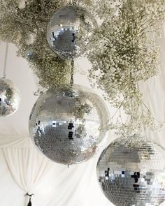 three silver disco balls hanging from a ceiling with baby's breath flowers in them