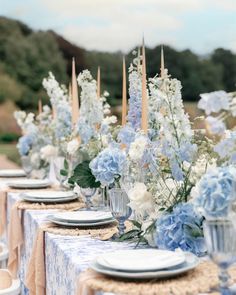 the table is set with blue and white flowers in vases, plates and napkins