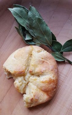 a piece of bread sitting on top of a wooden table next to a green leaf