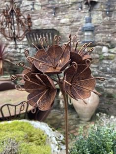 a metal flower sculpture sitting on top of a table next to a chair and potted plant