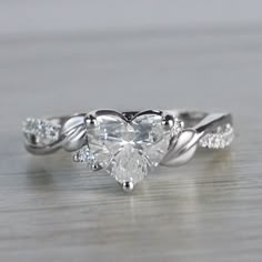 a heart shaped diamond ring on top of a wooden table with leaves and diamonds around it