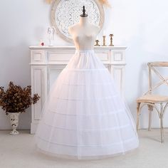 a white wedding dress is on display in front of a dresser and chair with flowers