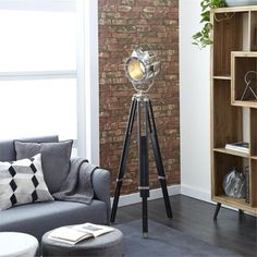 a living room with a gray couch and a black tripod floor lamp in front of a brick wall