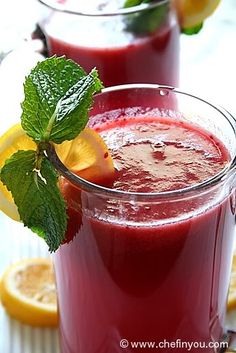 two glasses filled with red liquid and garnished with lemons on the side