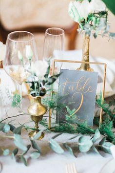 the table is set with gold vases, greenery and a chalkboard sign